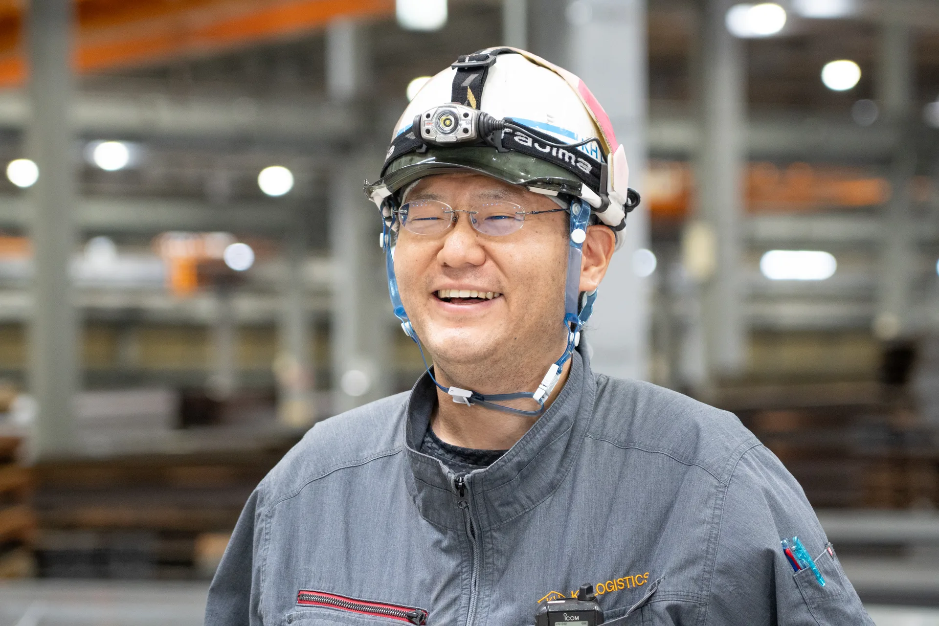 ヘルメット姿の男性社員が、倉庫でカメラのほうを見ている