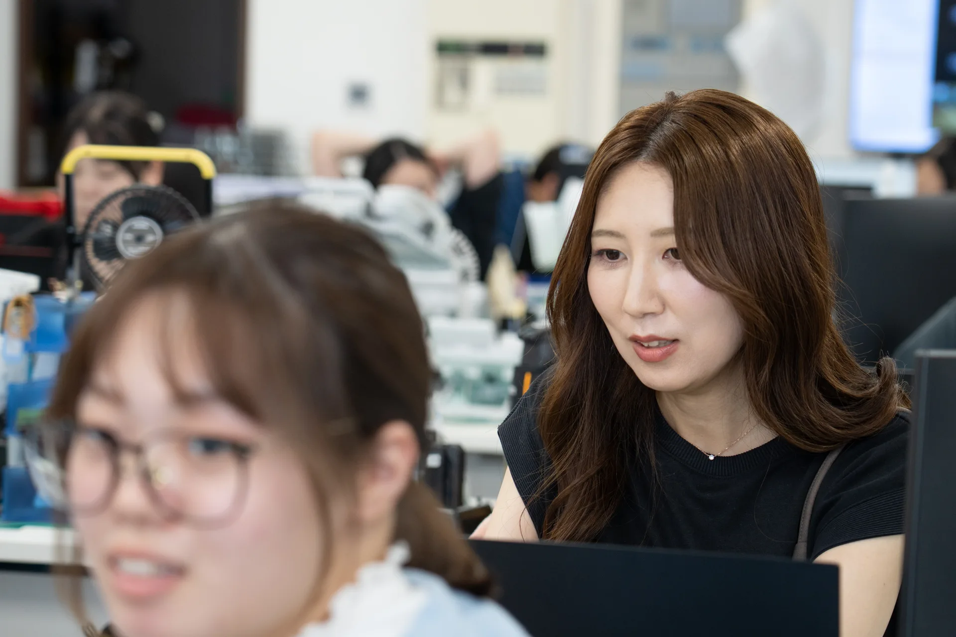オフィスでPCモニターを見ながら、女性社員同士が話している